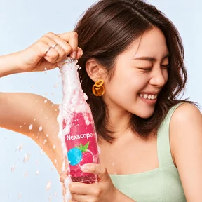Smiling model in a mint-green top opening a pink Nexscope sparkling drink
